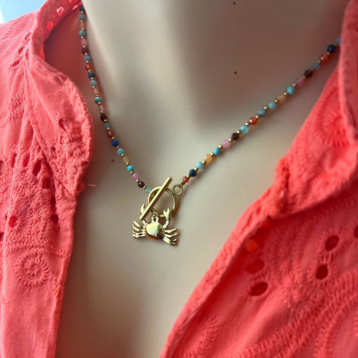 Modelo llevando el collar artesanal Cangrejo con Minerales de Algo de Olga: colgante cangrejo dorado con minerales naturales de colores sobre cadena dorada.