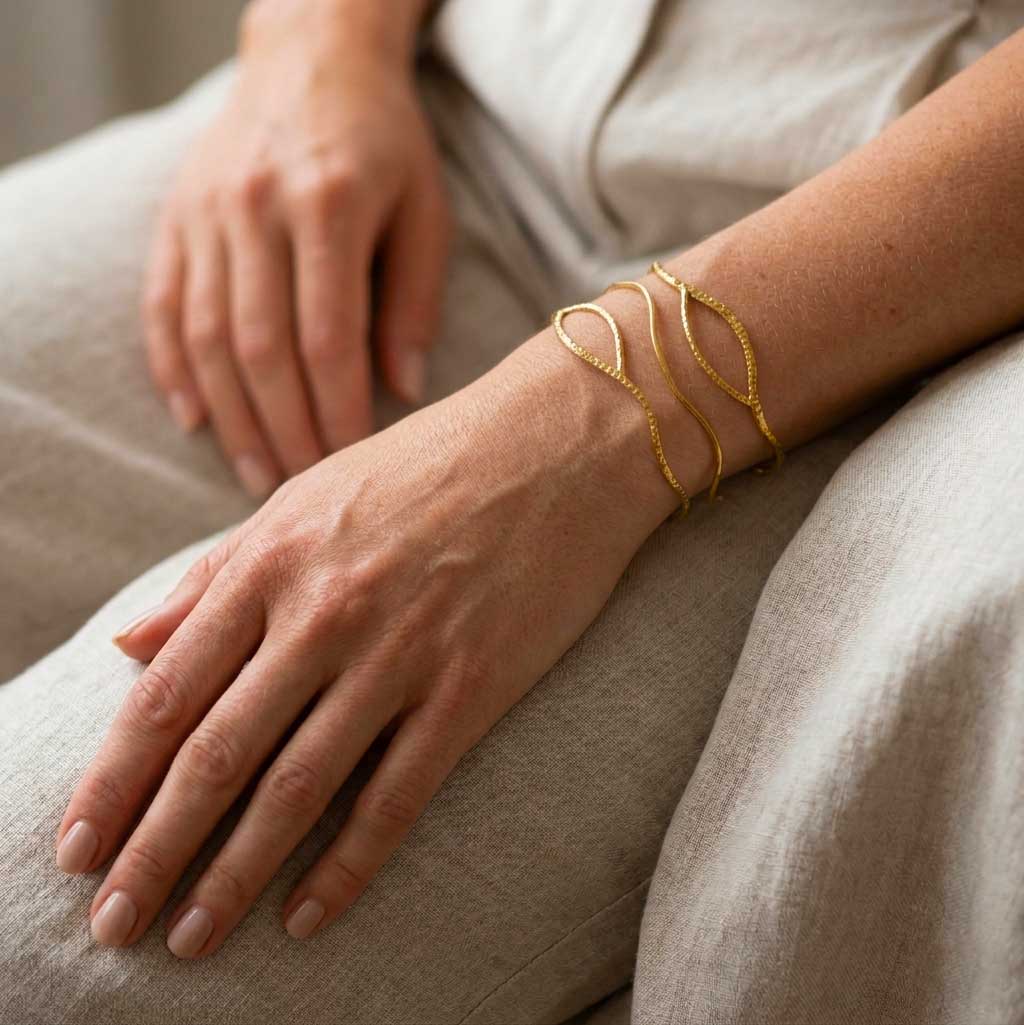 Brazalete abierto dorado con líneas onduladas y textura diamantada puesto en muñeca en una modelo con traje. Pulsera Anuska de Algo de Olga.