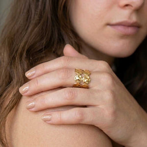 Mano con anillo Elena de acero dorado martillado con monedas superpuestas y uñas en tono nude.