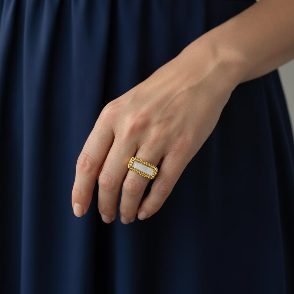 Mano con anillo de acero dorado y nácar sobre vestido azul marino