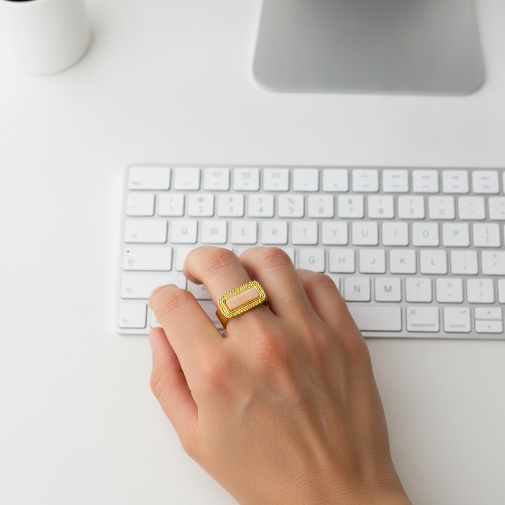 Mano con anillo de acero dorado y piedra del sol escribiendo en un teclado