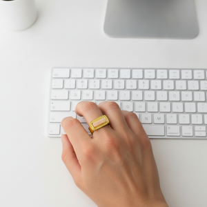 Mano con anillo de acero dorado y piedra del sol escribiendo en un teclado