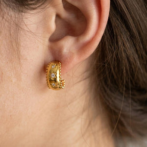 Oreja con pendiente semi aro Nieves dorado con estrellas en relieve y circonitas blancas puestos en una modelo.