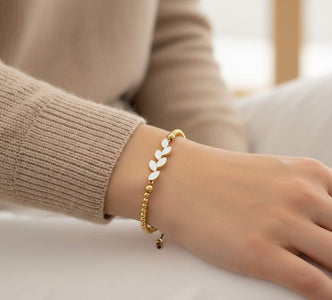Pulsera hecha a mano en acero dorado con rama de hojas de esmalte blanco y bolitas doradas.  Ajustable a cualquier muñeca.