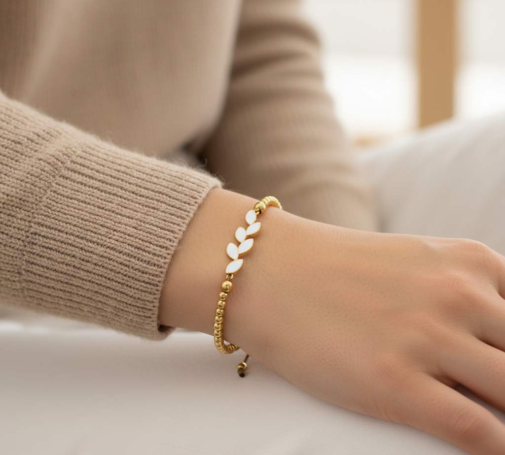 Pulsera hecha a mano en acero dorado con rama de hojas de esmalte blanco y bolitas doradas.  Ajustable a cualquier muñeca.
