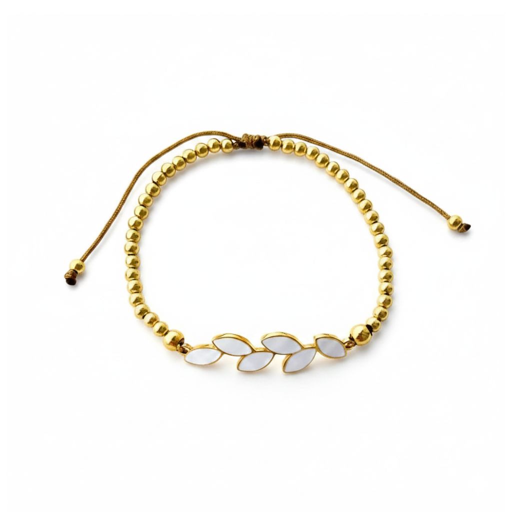 Pulsera ajustable de acero dorado con bolitas y rama de seis hojas de esmalte blanco, sobre fondo blanco