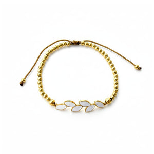 Pulsera ajustable de acero dorado con bolitas y rama de seis hojas de esmalte blanco, sobre fondo blanco