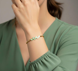 Pulsera ajustable de acero dorado con bolitas y rama de seis hojas de esmalte verde menta, sobre muñeca de mujer