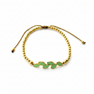 Pulsera ajustable de acero dorado con bolitas y rama de seis hojas de esmalte verde menta, sobre fondo blanco.